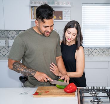 A loving couple preparing food with red and green peppers in a modern kitchen.