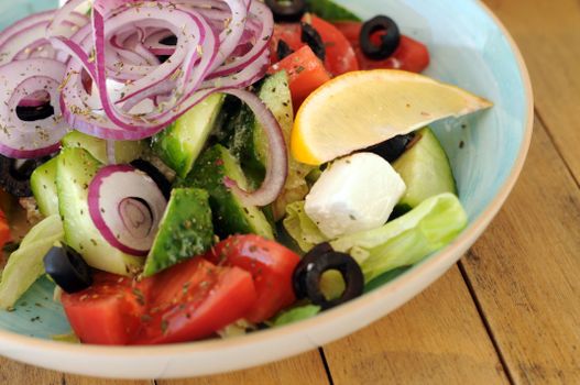 A vibrant bowl of Greek salad with fresh vegetables, feta cheese, and a lemon slice.
