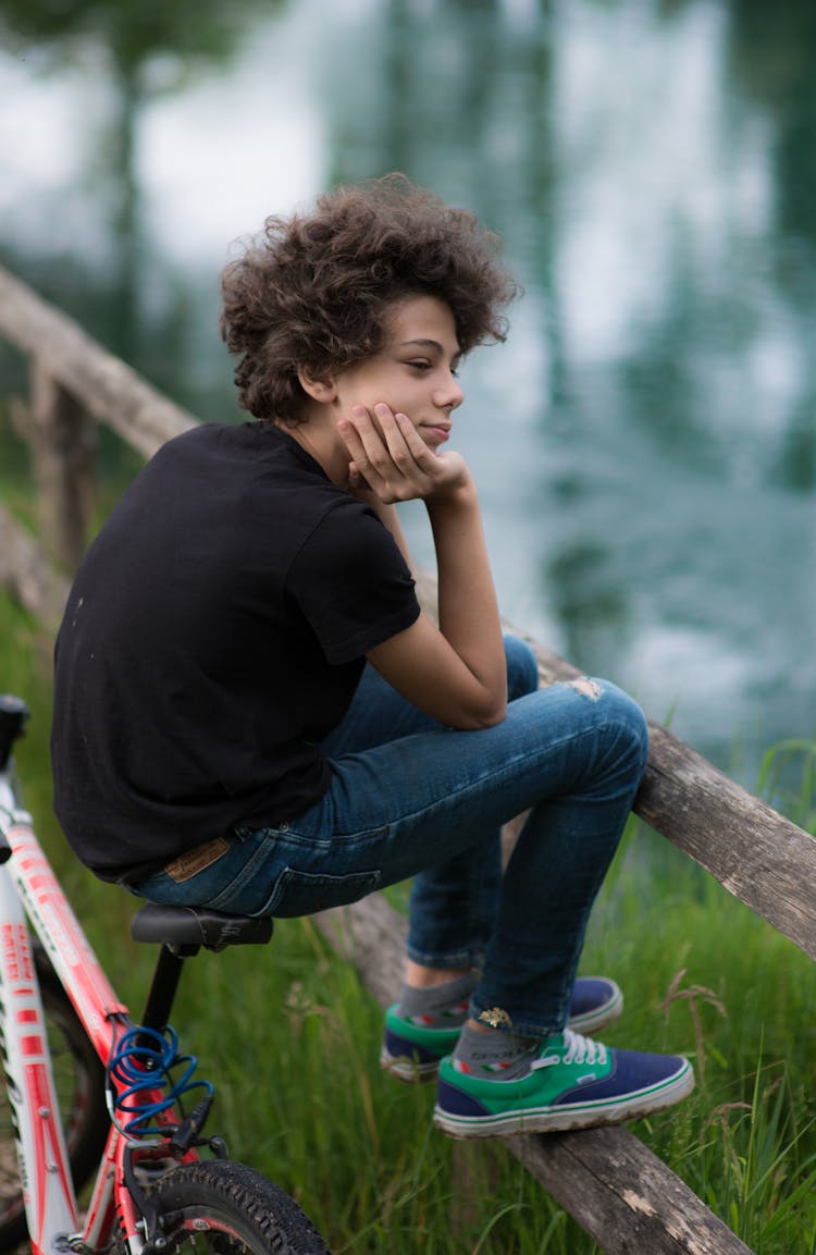 Young Boy Sitting On A Bike Near Water 