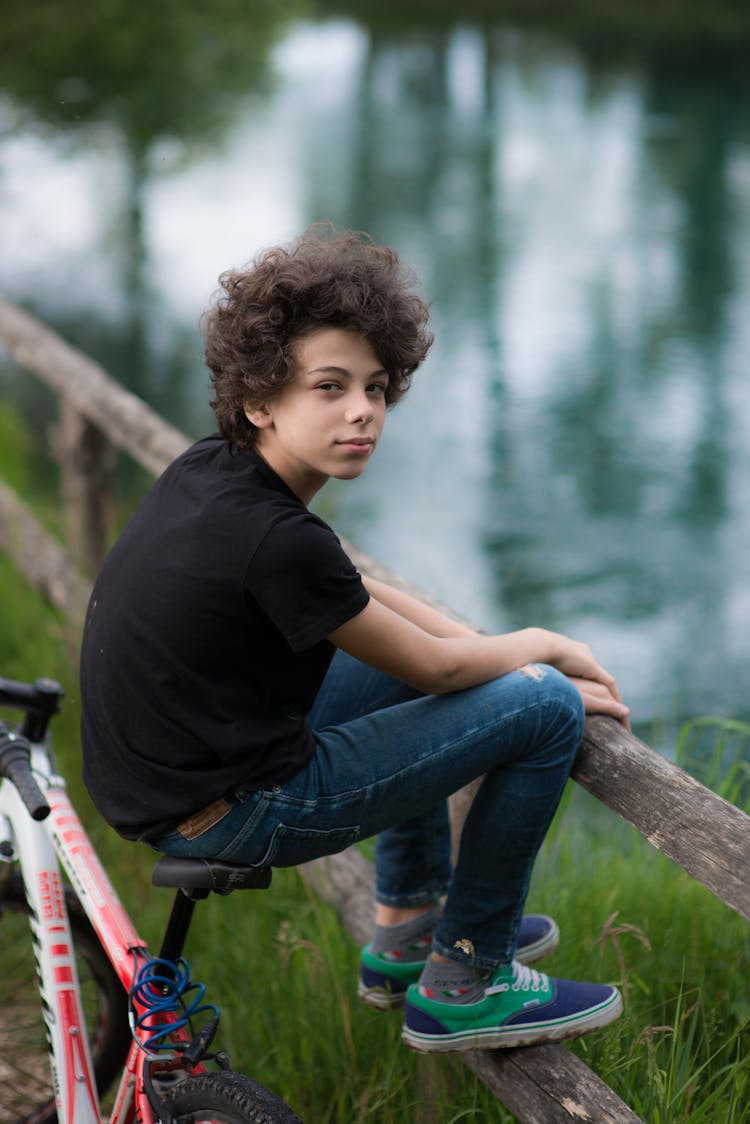 Young Boy Sitting On A Bike Near Water 