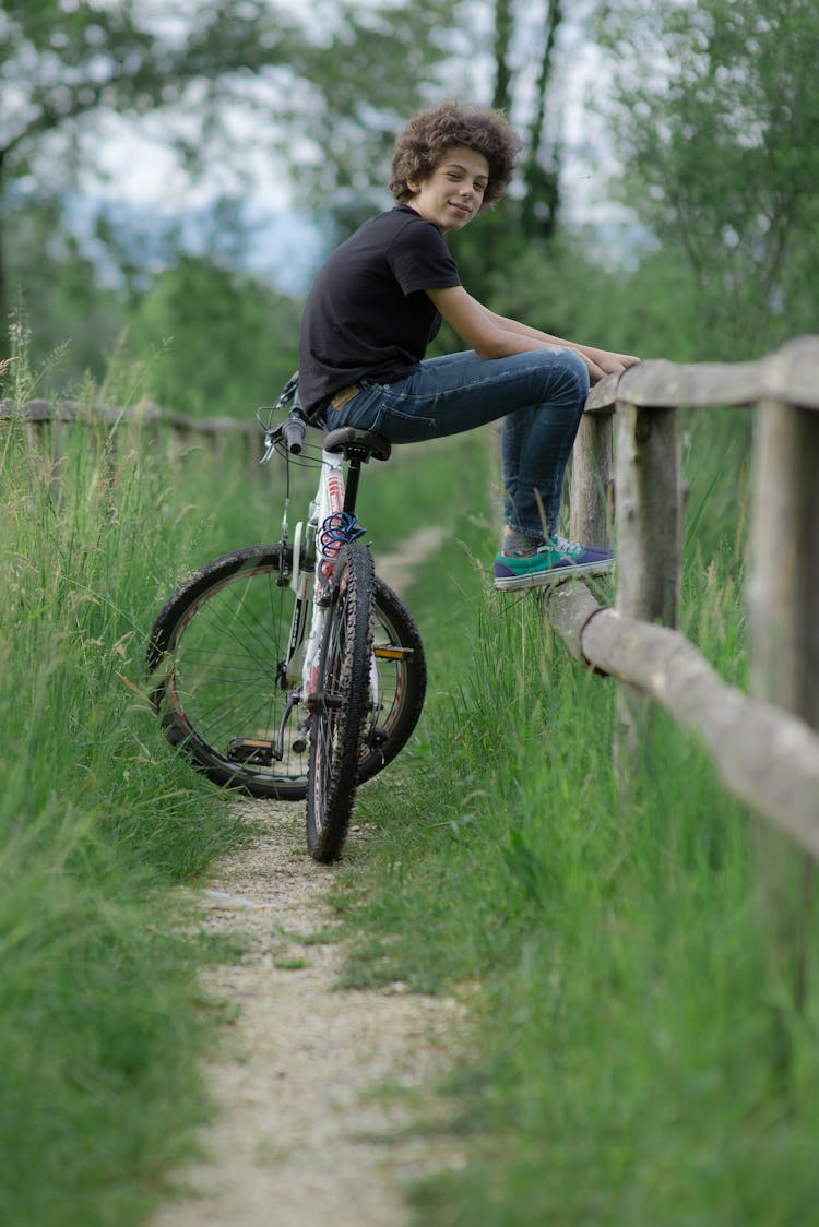 Young Boy Sitting On A Bike And Leaning Against A Fence