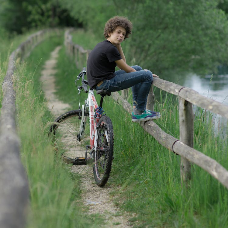 Young Boy Sitting On A Bike Near Water 