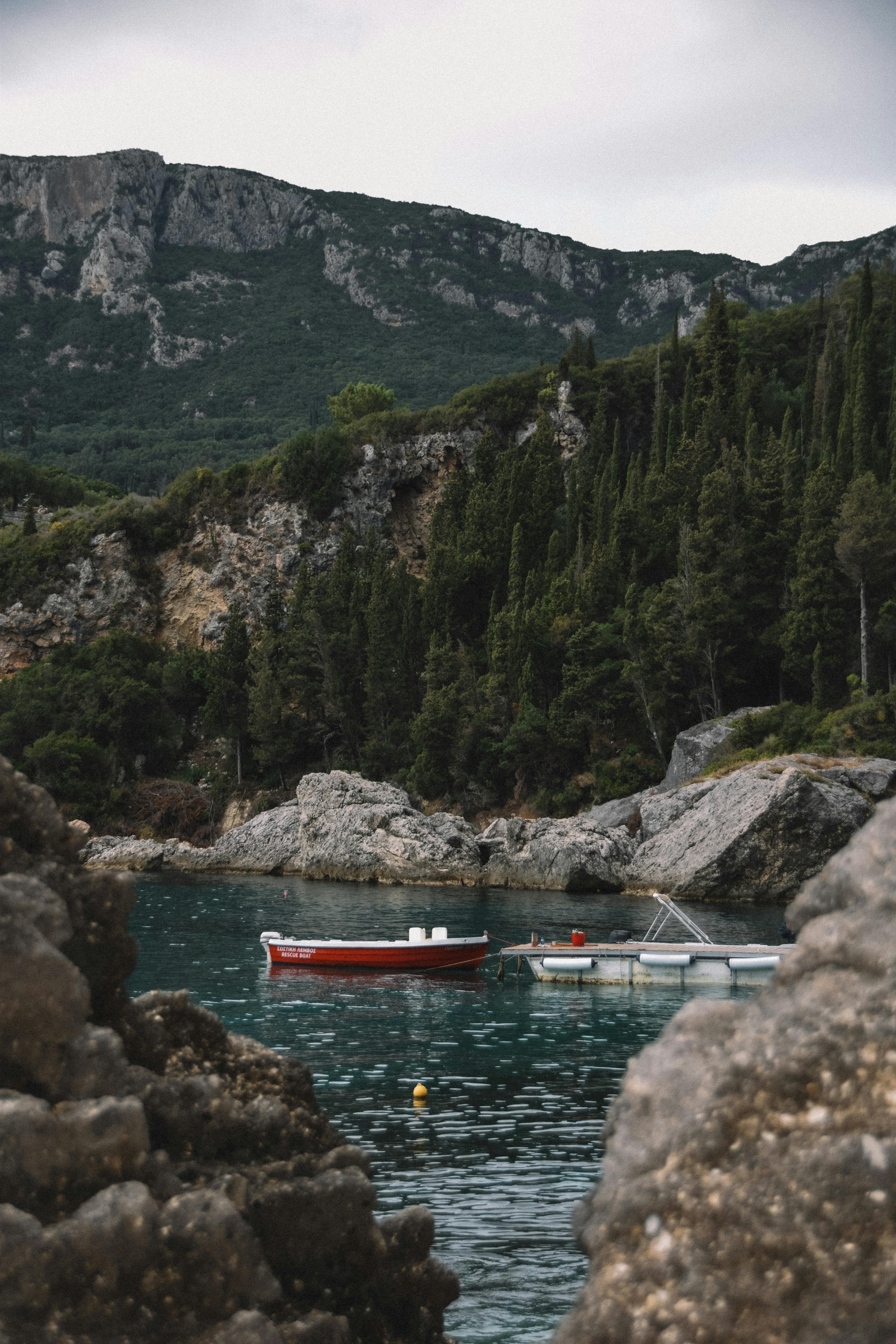 A tranquil scene of a boat docked by a rocky shore, with lush greenery and towering mountains.