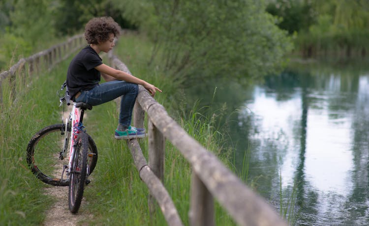 Young Boy Sitting On A Bike Near Water 