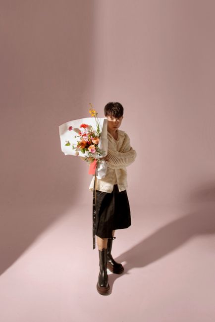 Stylish woman in a skirt with a bouquet of flowers in a minimalist setting.