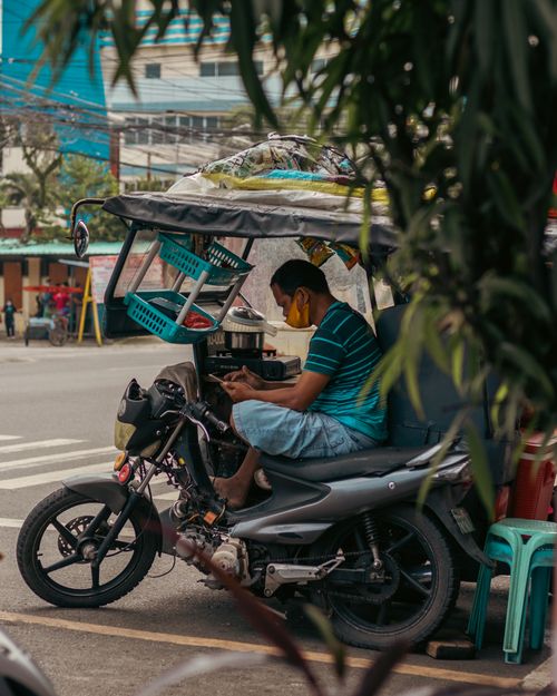 Free Driver wearing a face mask uses a smartphone while sitting in a tricycle in Davao City street. Stock Photo