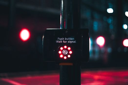 A close-up of a glowing pedestrian crossing button with red lights at night.