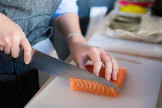 Close-up of a chef's hands slicing fresh salmon for sushi on a cutting board indoors.