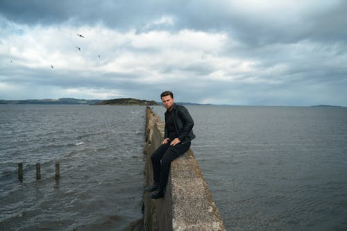 Man Sitting on a Concrete Breakwater on the Shore 