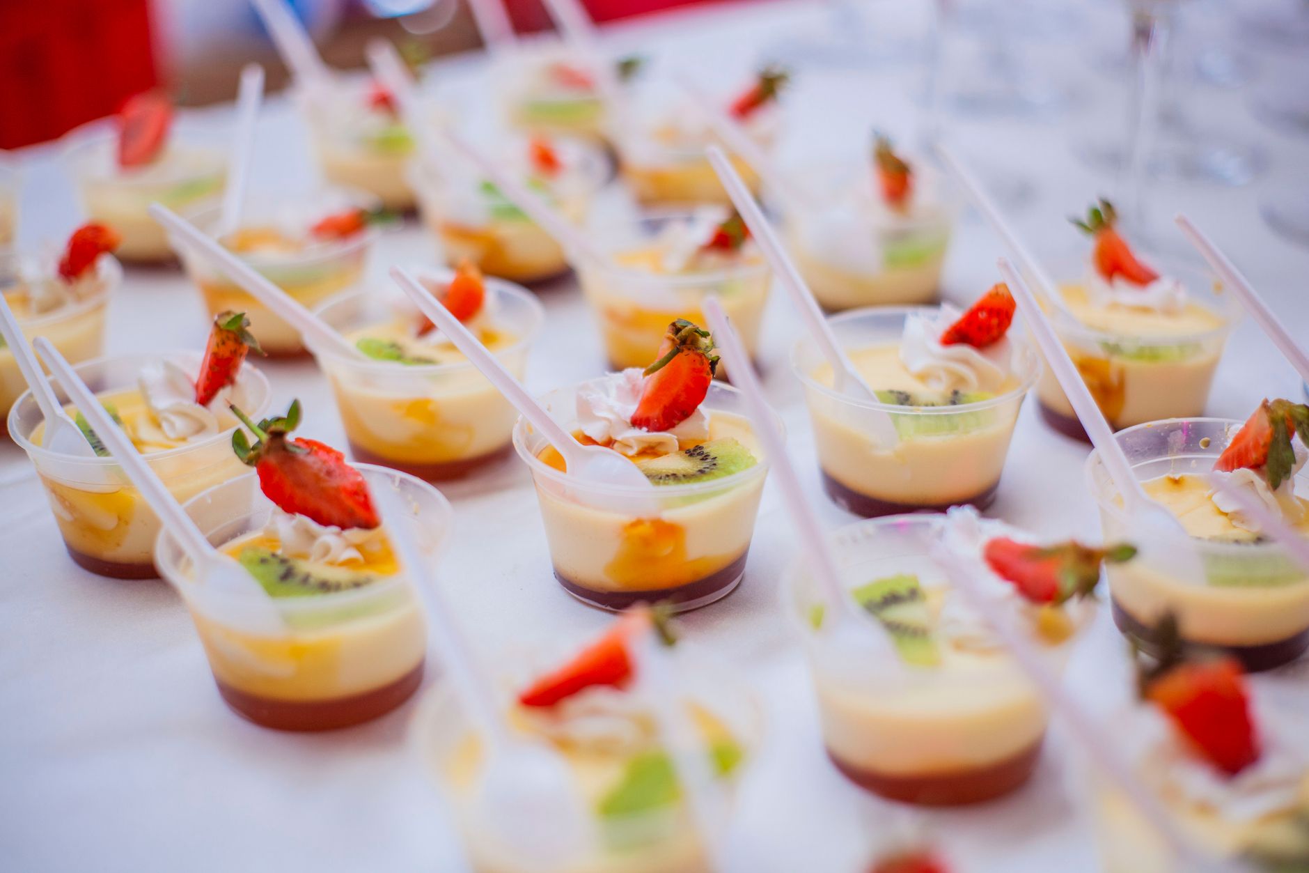 Close-up of vibrant fruit custard desserts with strawberries and kiwi in plastic cups.