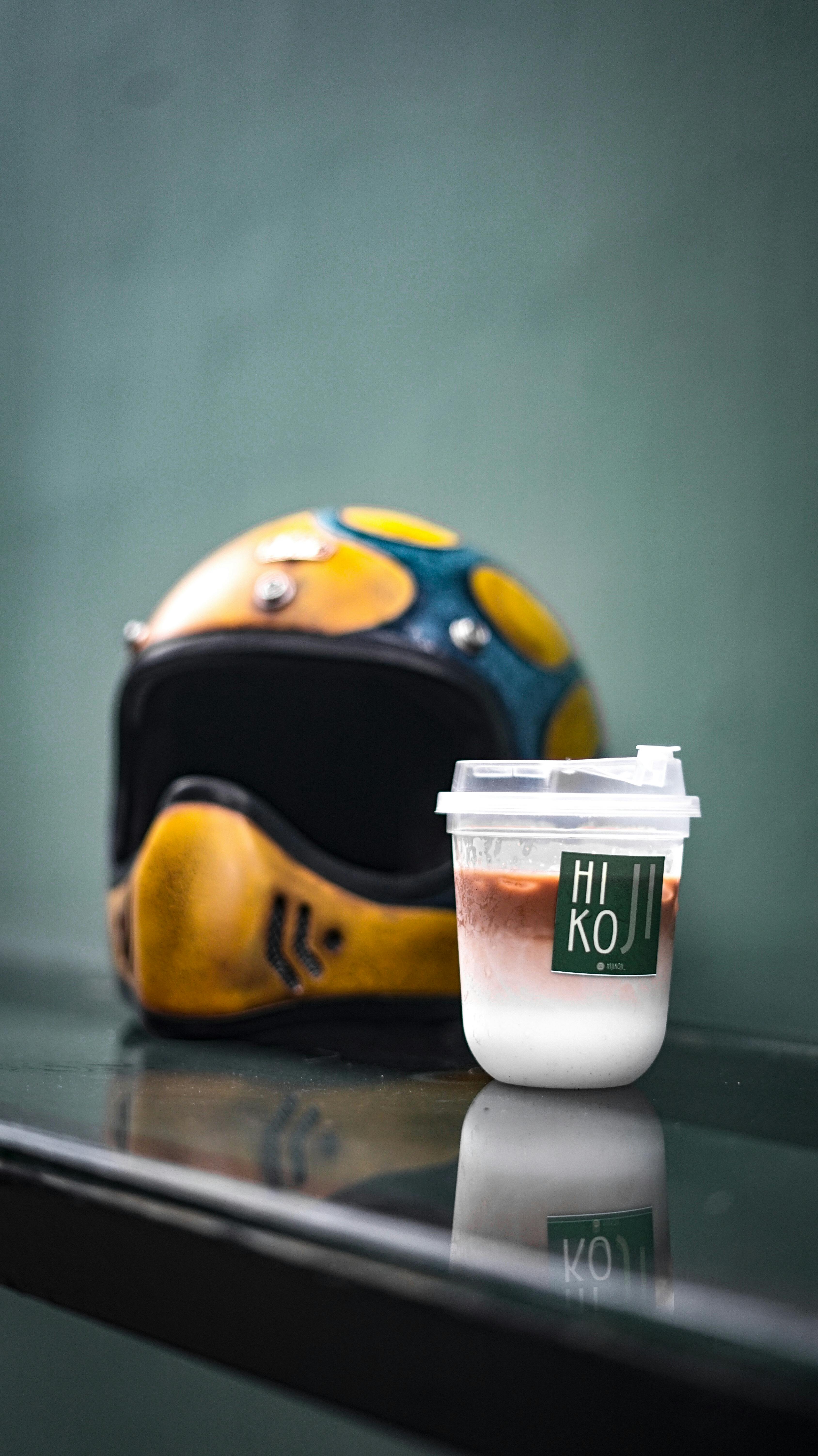 A colorful motorcycle helmet and a cold drink in a plastic cup on a reflective surface.