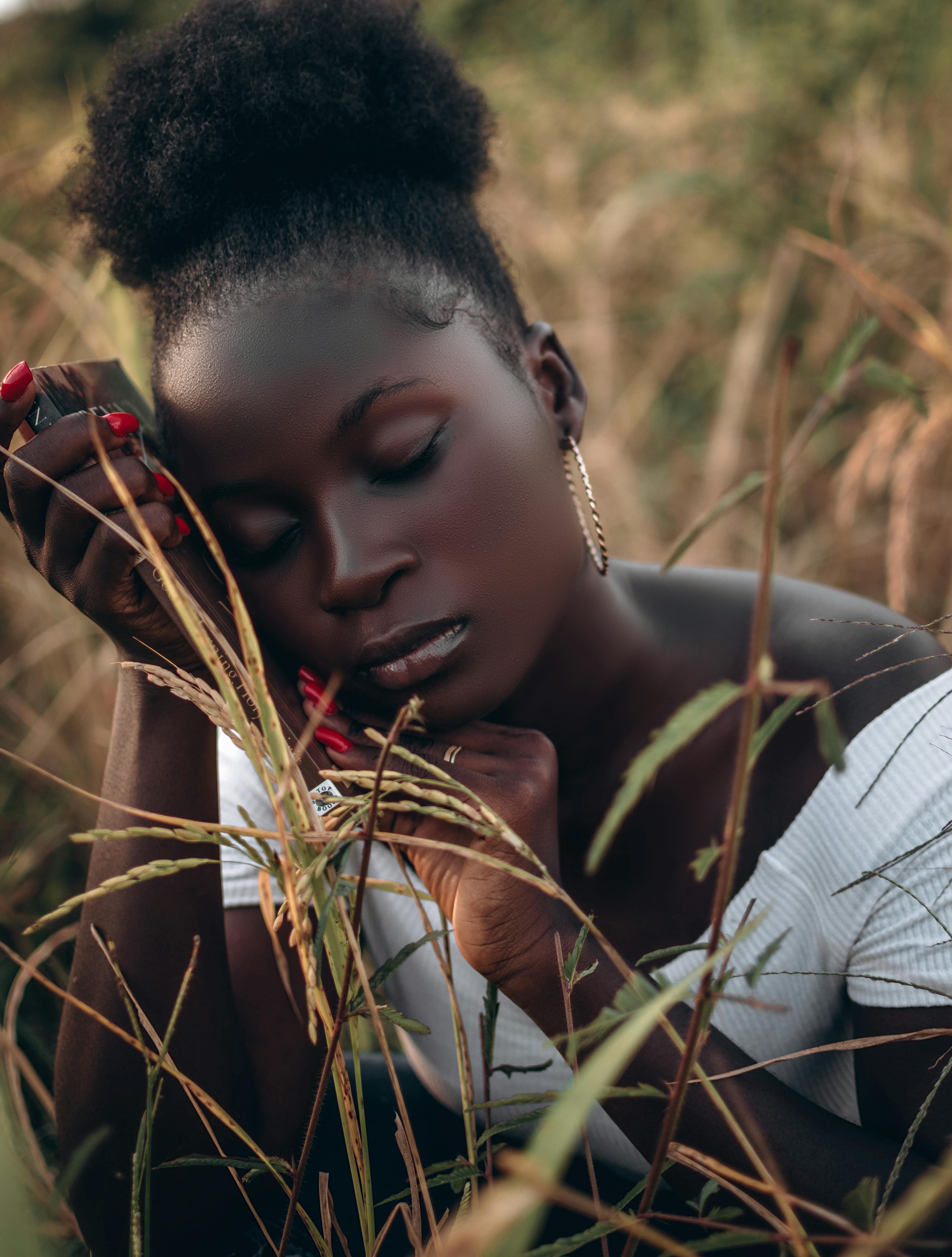 Elegant fashion portrait of a woman with eyes closed in a rural Nigerian hayfield, conveying tranquility and natural beauty.