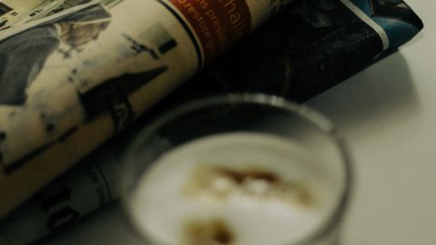 A close-up of a folded financial newspaper with a glass of espresso on a table.