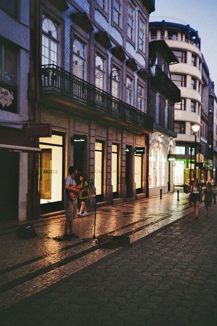 A street musician playing guitar in a quaint city street at twilight, capturing urban nightlife charm.