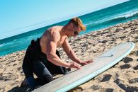 Man Waxing Surfboard on Beach