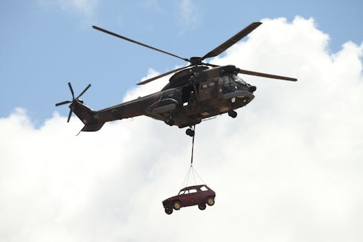 A helicopter transporting a car in midair under a clear blue sky.