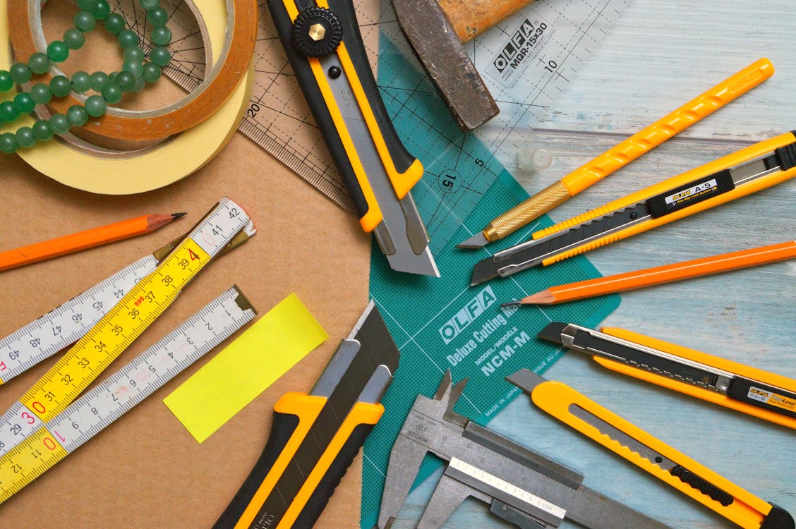 Assorted-type-and-size Utility Cutters on Clear and Green Olfa Measuring Tool Near Adhesive Tape Rolls