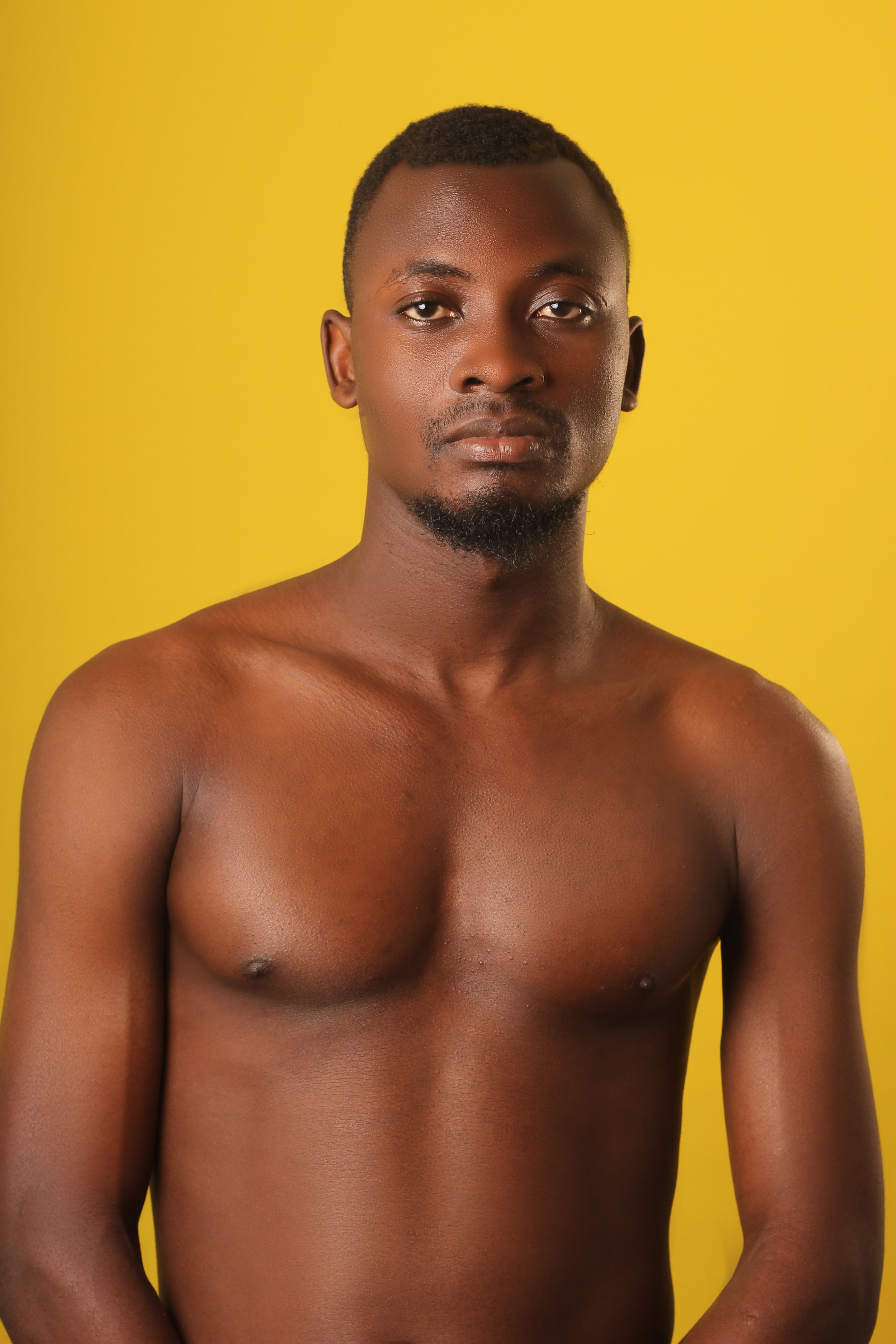 Studio portrait of an adult man standing shirtless against a vibrant yellow backdrop.