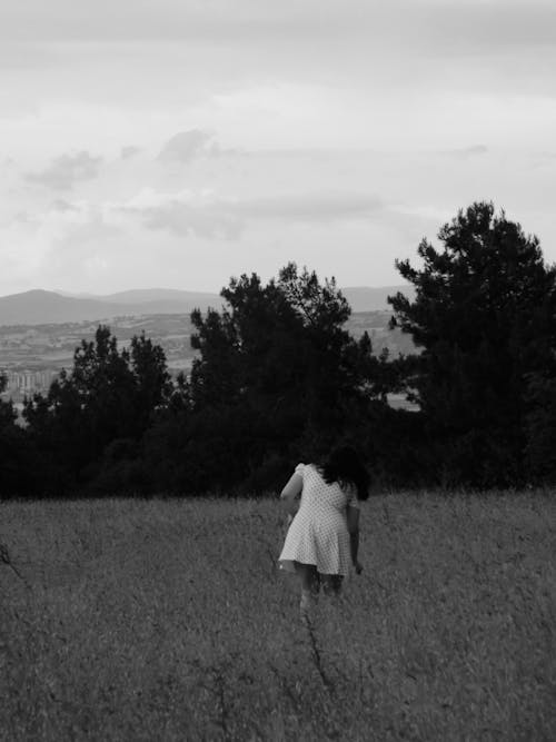 Grayscale Photo of a Woman in Dress Standing on Grass Field