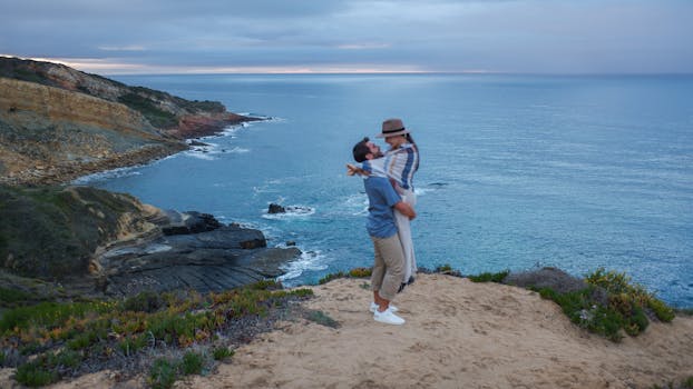 A couple embraces on a scenic cliff with ocean views, showcasing romance and nature's beauty.