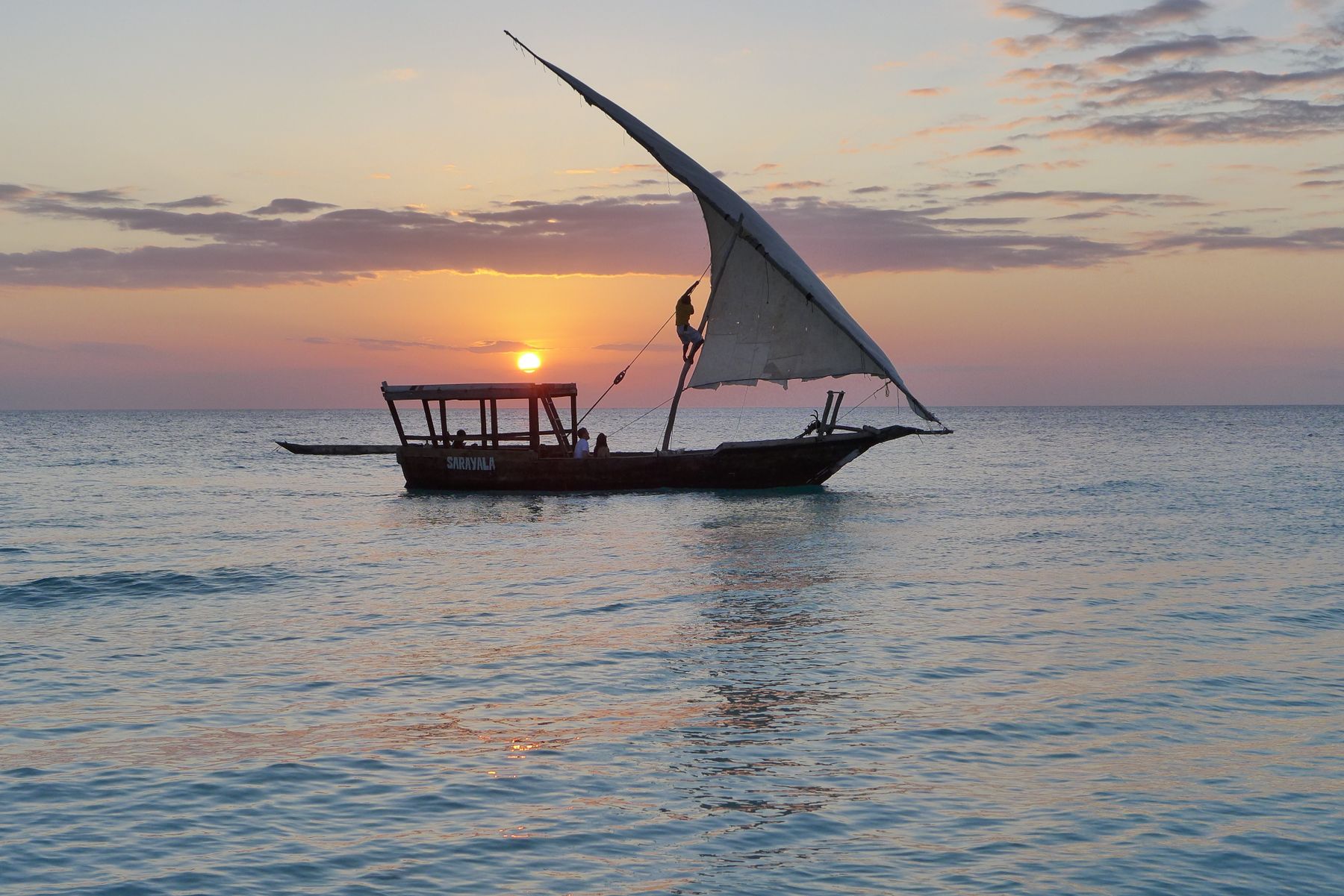 Guests and crew sailing a traditional dhow across the Indian Ocean at sunset off Zanzibar, Tanzania