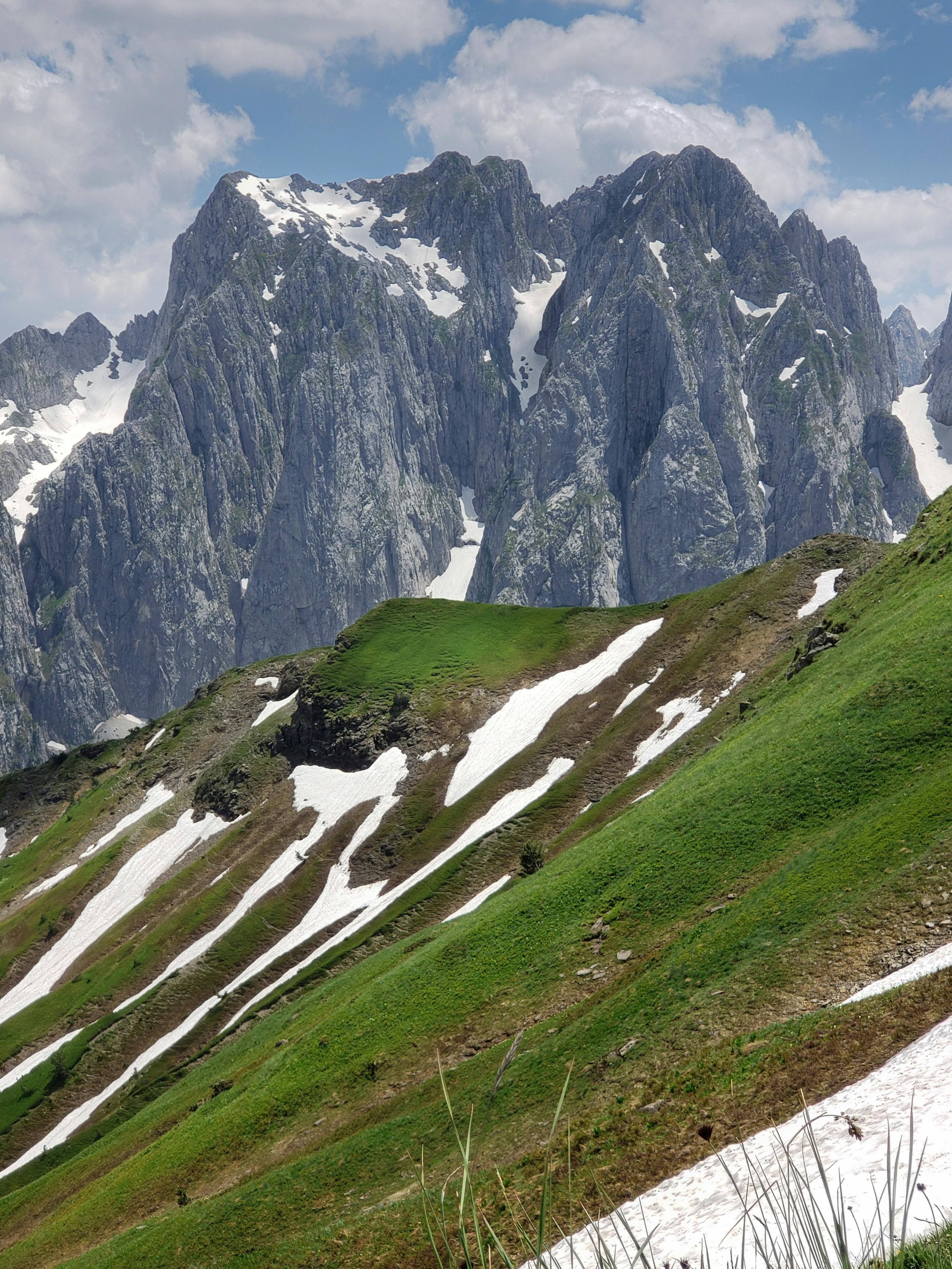 Dramatic view of towering snow-capped mountains and lush green meadows in Lëpushë, Albania.