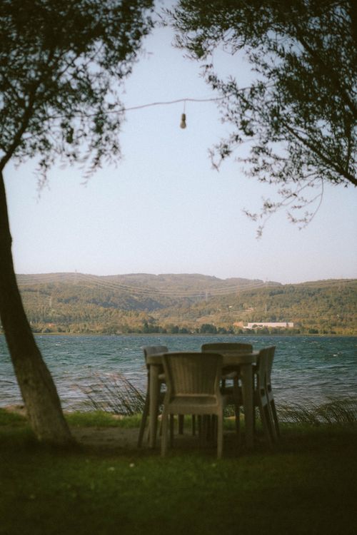 Free A serene lakeside scene in Sapanca, Turkey, featuring chairs and table under lush trees. Stock Photo