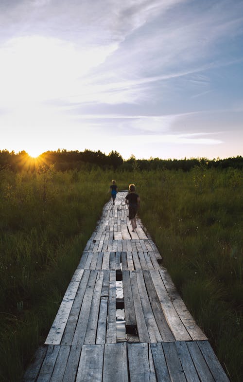 Two Kids Running on Wooden Pathway during Sunset