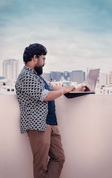 一名男子在班加罗尔城市天际线的背景下，于屋顶上使用笔记本电脑工作