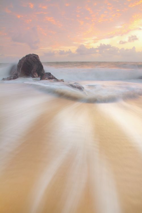 Free Peaceful coastal scene with blurred waves at sunrise, highlighting a serene rock formation. Stock Photo