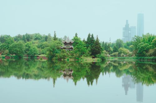 Free Peaceful city park with pagoda, skyscraper reflections in a calm river surrounded by lush greenery. Stock Photo