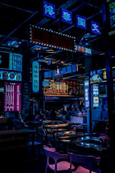 Colorful neon signs illuminate an Asian indoor market at night, creating a vibrant atmosphere.