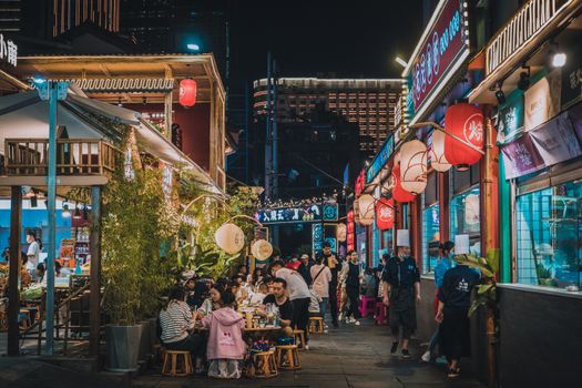 Explore the vibrant atmosphere of an outdoor Asian street market bustling with people and colorful lights at night.