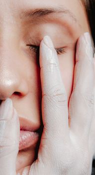 Close-up of a woman's face with gently closed eyes and painted hand touching her cheek.
