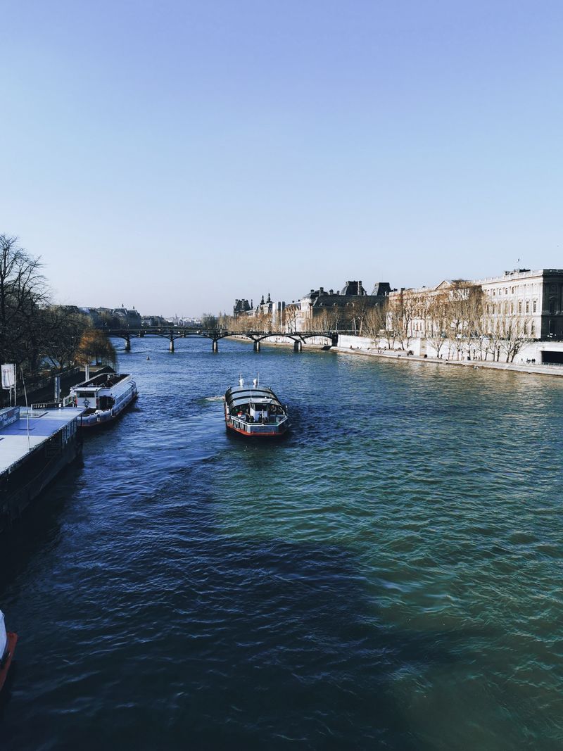 Tranquil river scene with several boats moving under a clear blue sky during the day