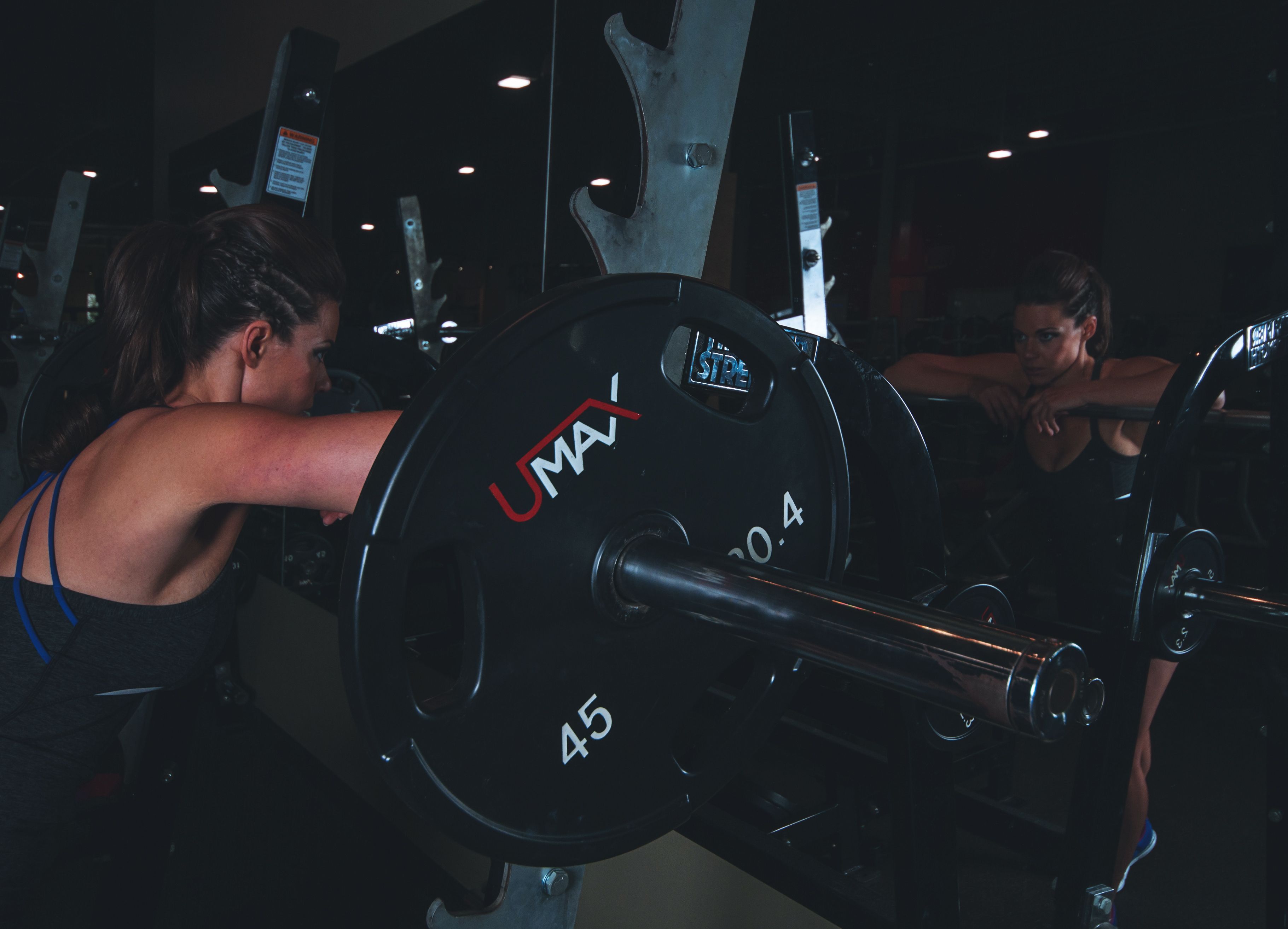 Woman in gym attire reflects in mirror while preparing for weightlifting session.