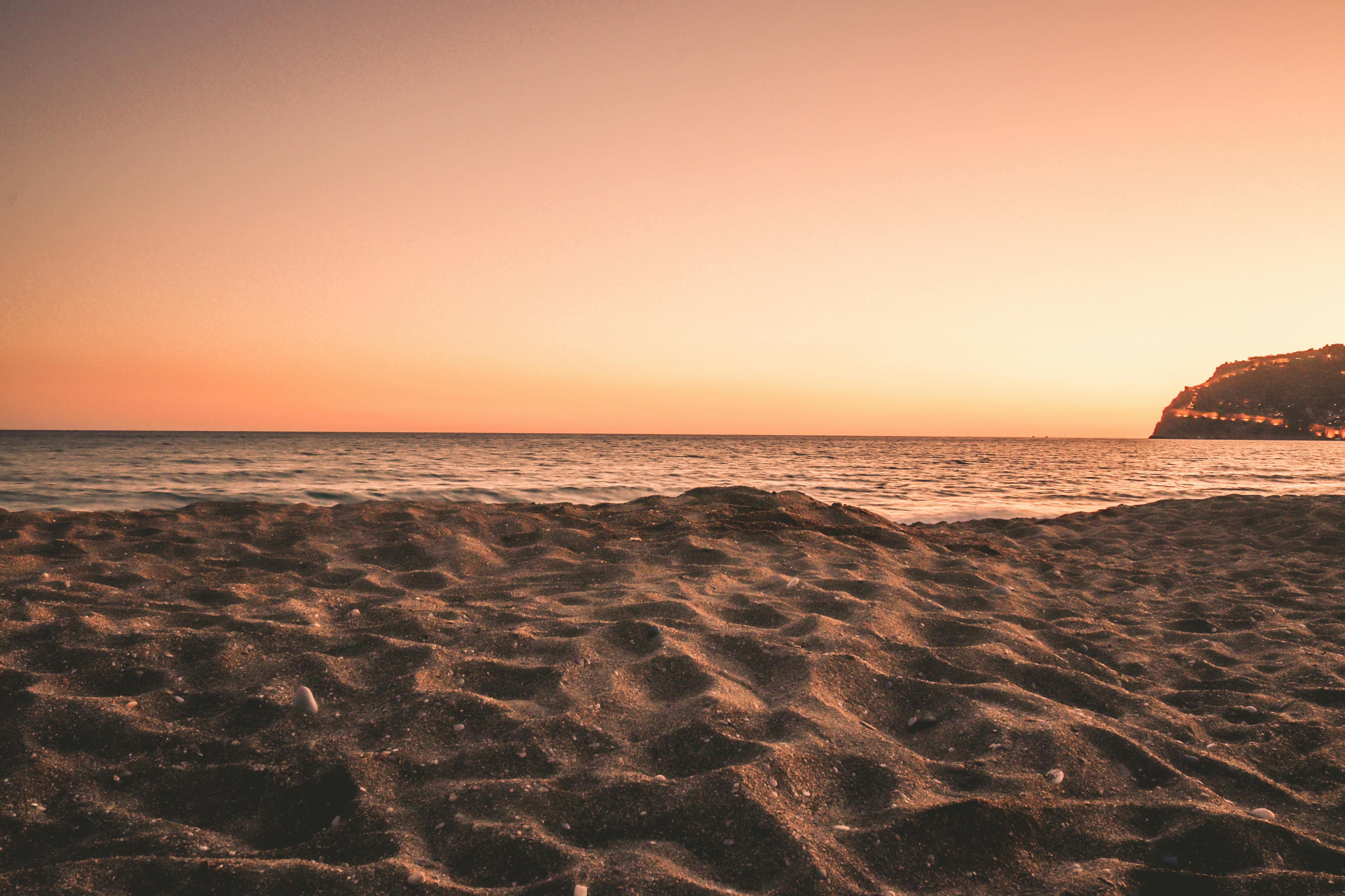 Una playa de arena serena al atardecer con un océano calmado y matices dorados en el cielo.