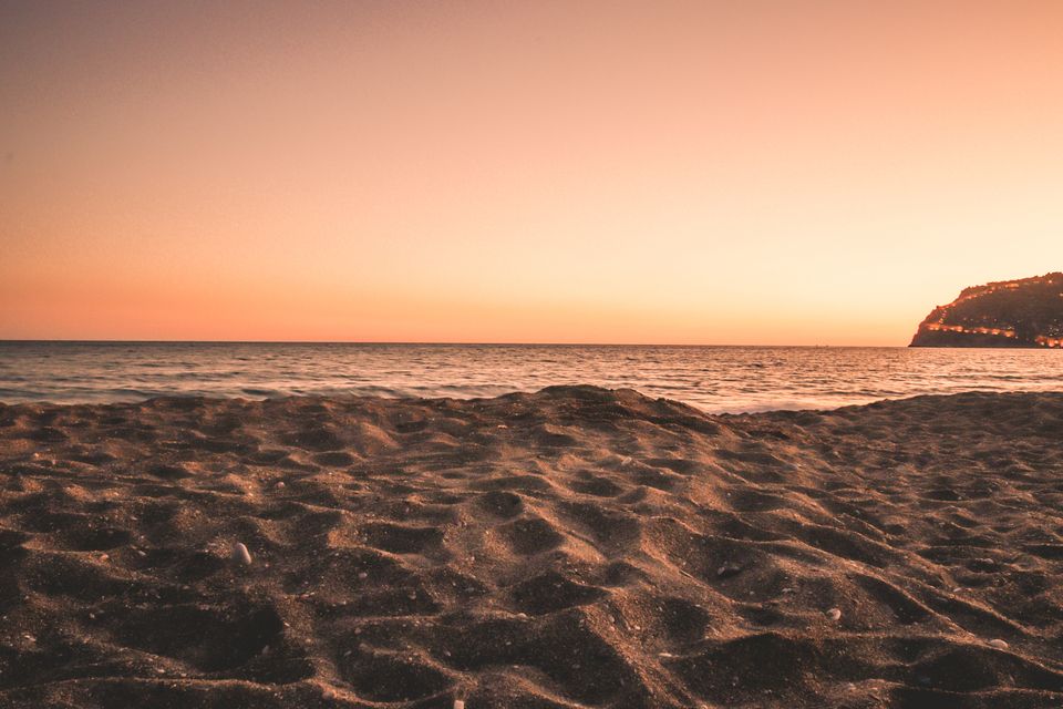 A serene sandy beach at sunset featuring a calming ocean and golden sky hues.