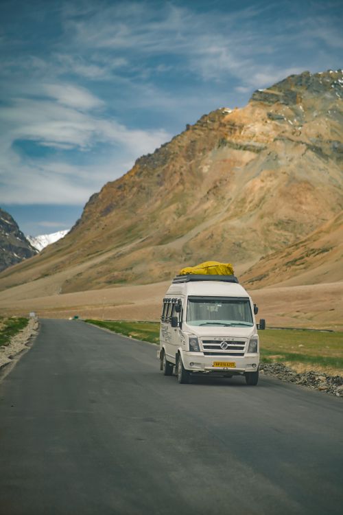 Free White van travels on a scenic road through the mountains of Leh, India, under a clear blue sky. Stock Photo
