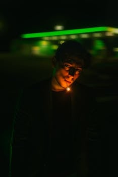A mysterious man poses at night with an illuminated matchstick, creating a dramatic effect.