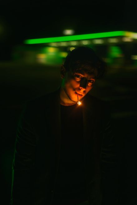 Man lighting a match on a green-lit street at night, photo by Vladislav Nahorny on Pexels