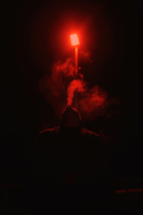 Free A mysterious silhouette against a glowing red light emitting smoke in the darkness. Stock Photo