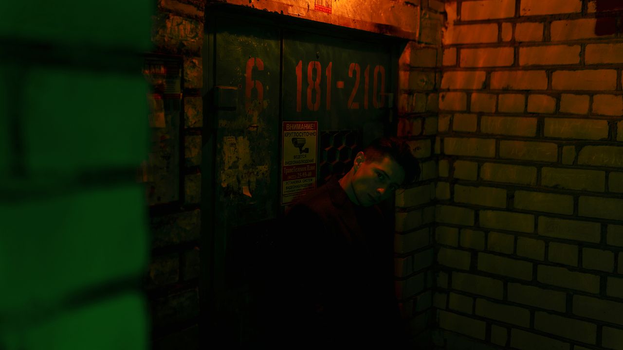 a man stands in a dimly lit urban alleyway surrounded by textured bric
