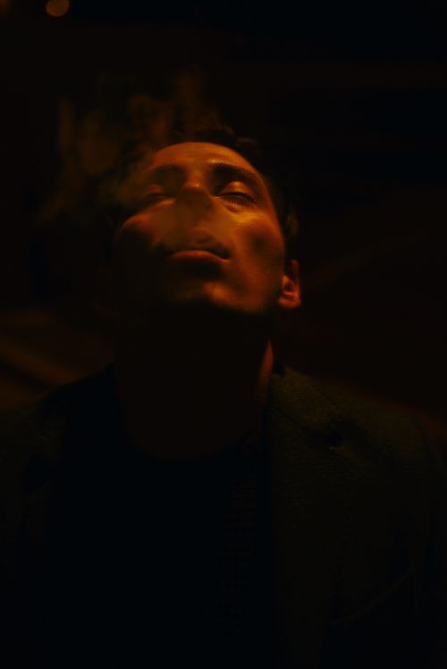 Free A deep and atmospheric portrait of a man exhaling smoke, set in dim lighting. Stock Photo