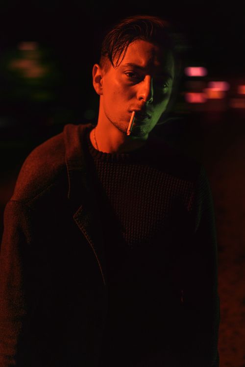 Free Dramatic nighttime portrait of a young man smoking under colorful lights. Stock Photo
