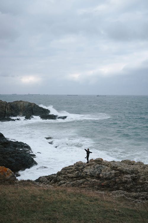 Person Standing on Rock Formation Near Sea