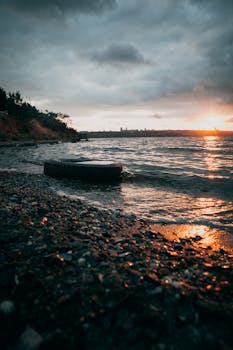 Dramatic sunset over a rocky lakeshore with waves and a tire in view.