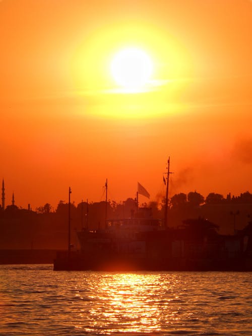 Ship Silhouette against Orange Sky and Yellow Sun Reflecting in Water