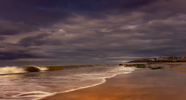 A serene beach view with dramatic clouds and gentle waves at dusk creating a tranquil atmosphere.