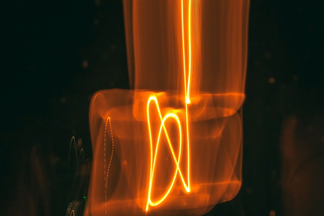 Long-exposure light painting drawing a looping ember-coloured line on black — photo by Mahdi Bafande on Pexels